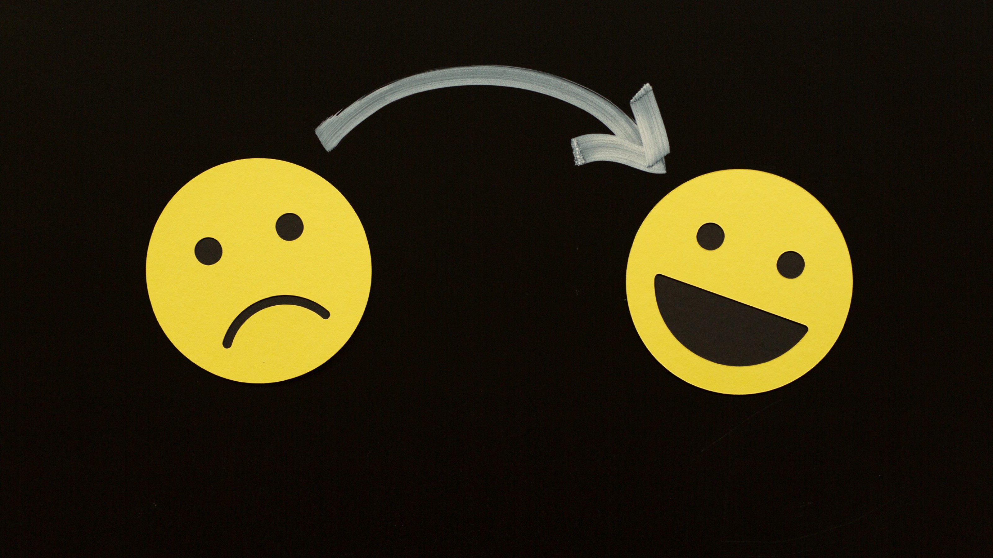 An arrow points from a sad yellow emoji face on the left to a happy yellow emoji face on the right against a black background.