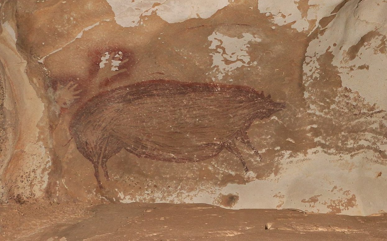 Ancient cave painting depicting animal figures, including what appears to be a bull and a bird, on a textured, brown and beige rock surface.