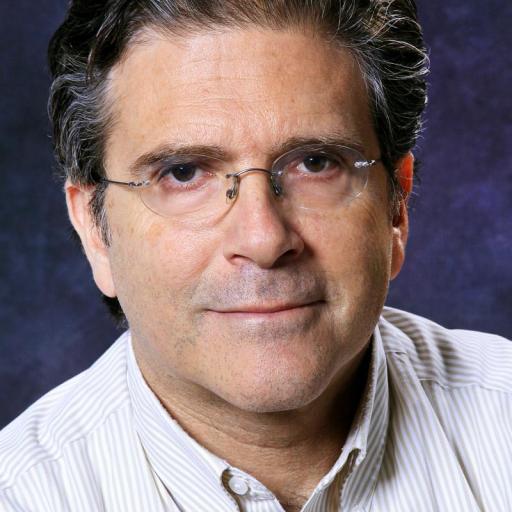 Middle-aged man with glasses, dark wavy hair, and a striped button-down shirt, posing against a dark, textured background.