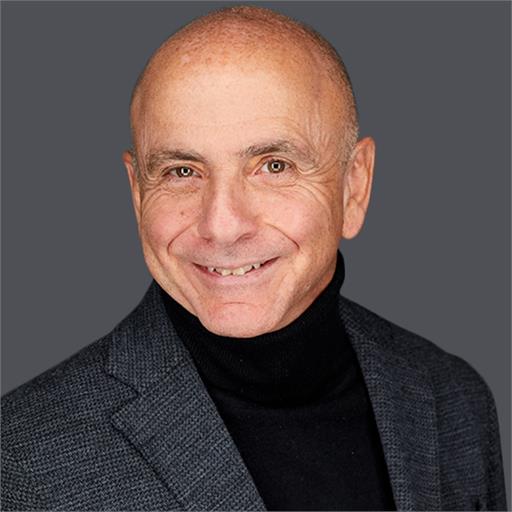 Bald man with light brown eyes, light skin, and a friendly smile, wearing a dark turtleneck and charcoal blazer, against a gray background.