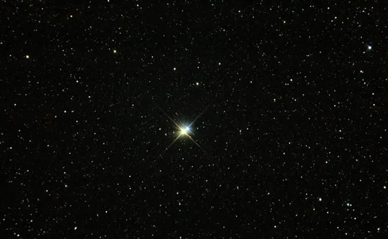 A bright star shining in a dark sky filled with numerous smaller stars. The larger star appears at the center with a noticeable twinkle effect.