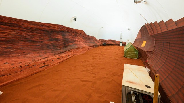 A room simulating a Martian landscape with red sand, rocky walls, a green tent, and NASA equipment.