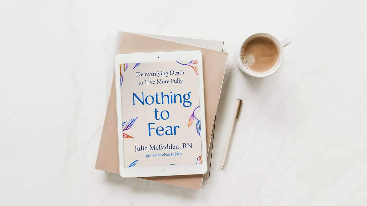 A tablet displaying the cover of the book "Nothing to Fear" by Julie McFadden, RN, lies on top of stacked books next to a pen and a cup of coffee on a white surface.