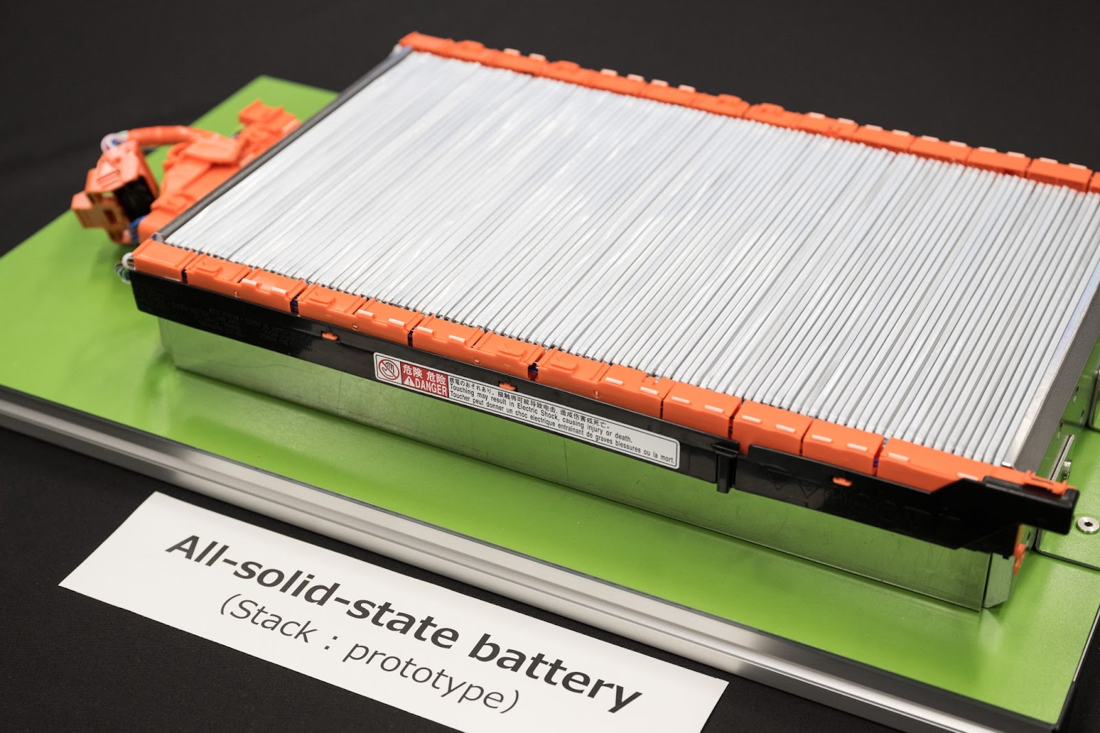 A prototype of an all-solid-state battery is displayed on a green surface, labeled with "All-solid-state battery (Stack: prototype).