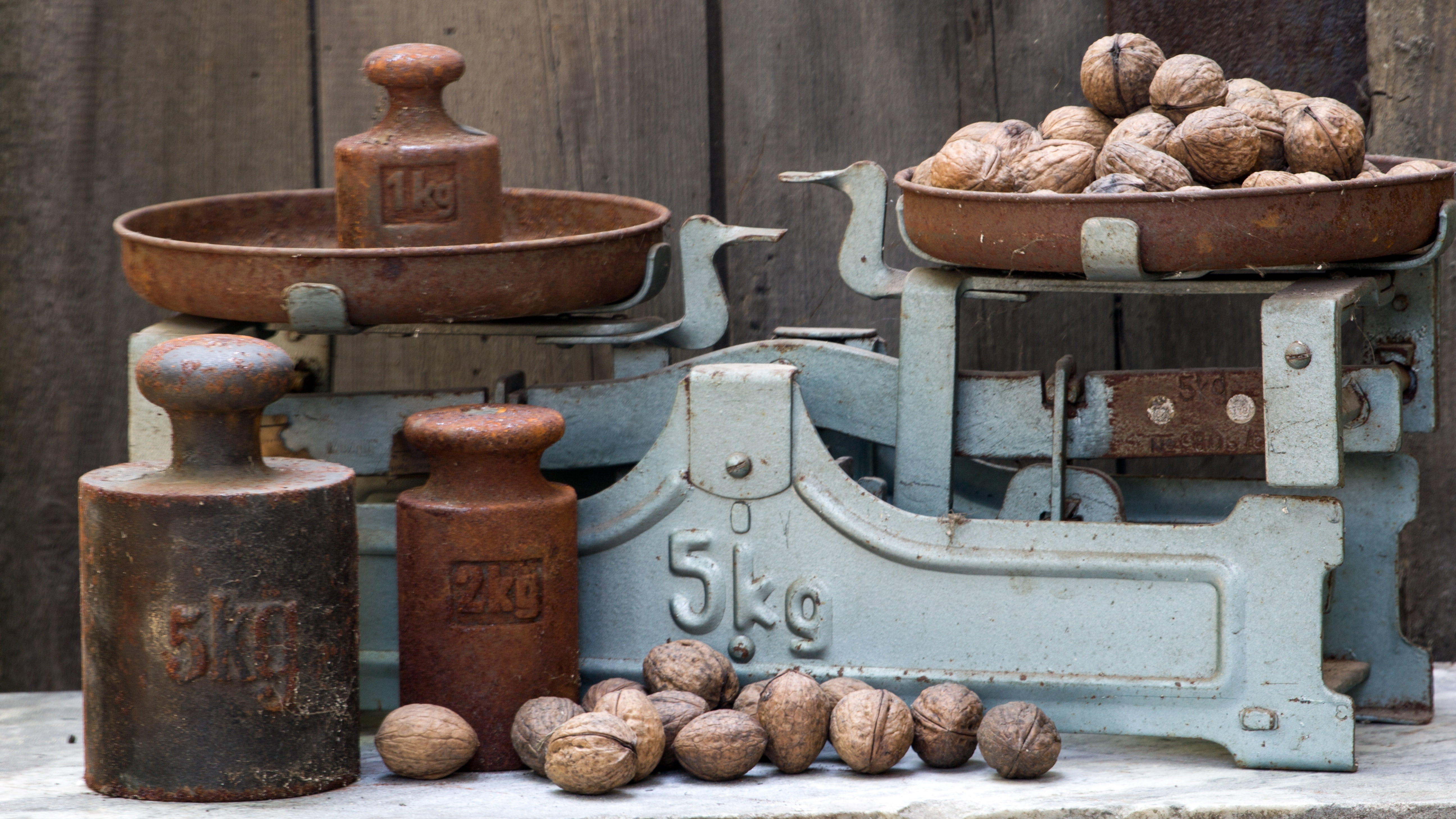 An old-fashioned scale with rusted weights in 1kg and 2kg, along with several walnuts on the scale and surrounding platform.