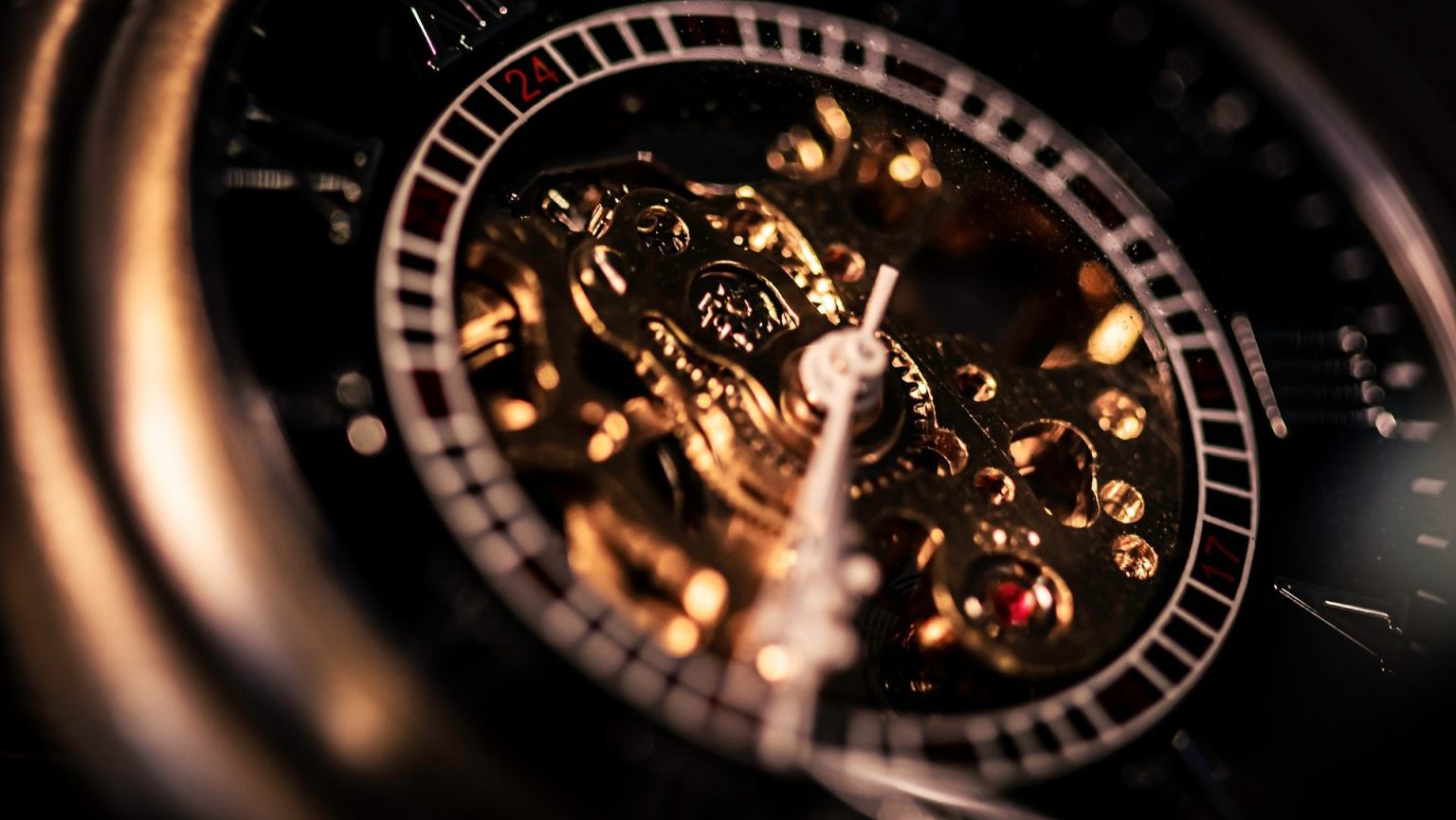 Close-up of a mechanical watch face with exposed gears and intricate details, highlighted by gold and dark tones. The minute and second hands are visible.