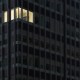 A high-rise office building at night with one illuminated corner office visible amidst the darkened windows, a lone workaholic burning the midnight oil.