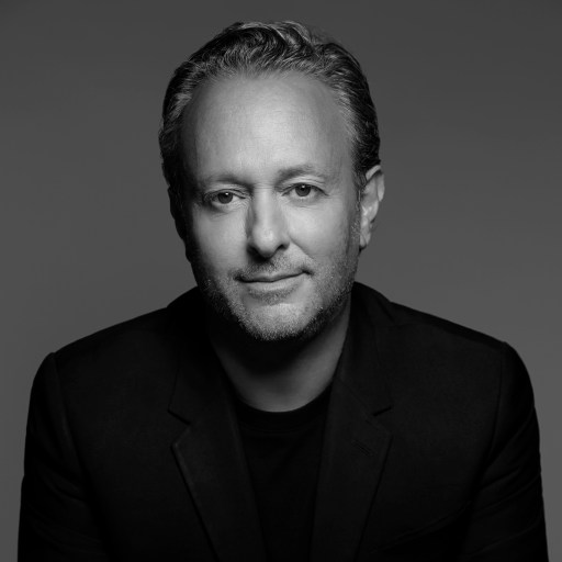 Black and white portrait of a middle-aged person with short, curly hair wearing a dark blazer, smiling slightly.