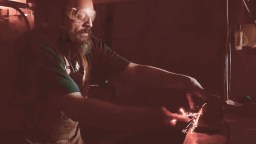 A person wearing safety goggles is using a tool to grind or cut metal, creating sparks in a dimly lit workshop.