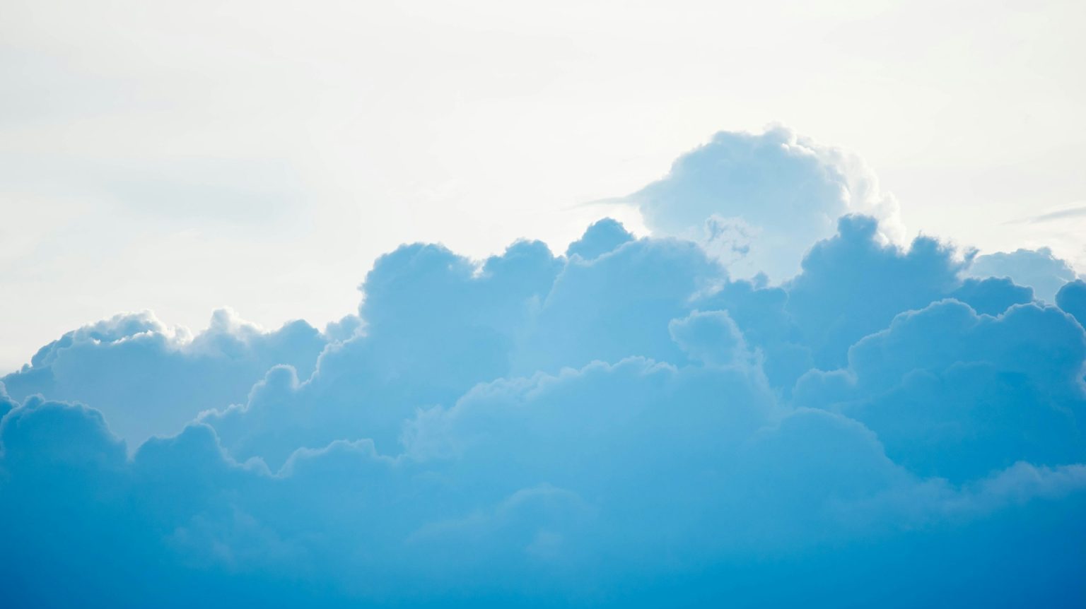 A clear blue sky with large, fluffy white clouds. The sunlight is softly illuminating the clouds from behind.