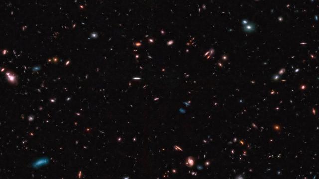 A deep-space image captured by the JWST showcases numerous galaxies of various shapes, sizes, and colors scattered across a dark background, potentially setting a new cosmic distance record.