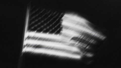 A blurred black-and-white image of an American flag, with the stars and stripes visibly distorted, subtly reflecting political polarization.