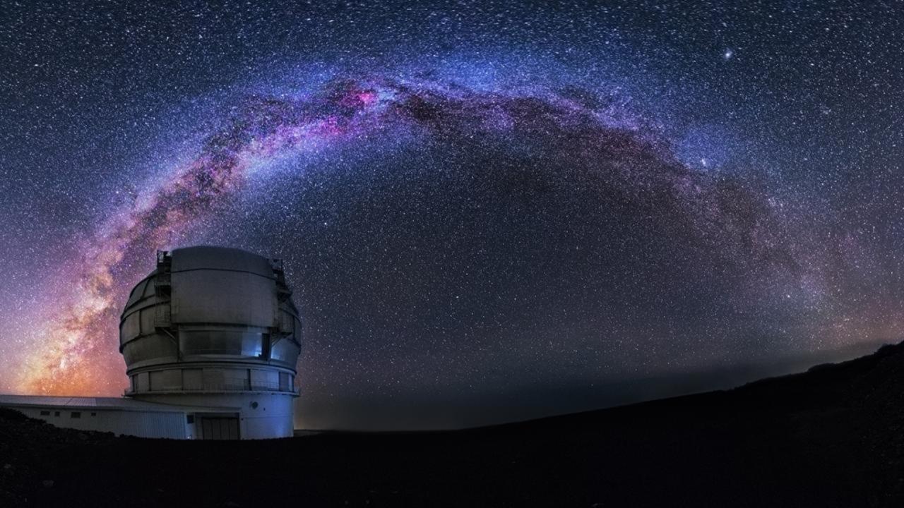 A large observatory dome beneath a starry night sky with the bright, colorful Milky Way arching overhead, marking it as one of the best astronomy locations on Earth.