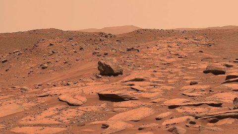 Rocky, reddish Martian landscape with scattered boulders and a hazy sky.