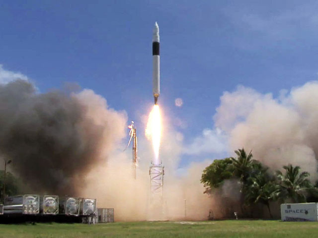 A rocket launching into a clear blue sky with smoke billowing around the launch site.