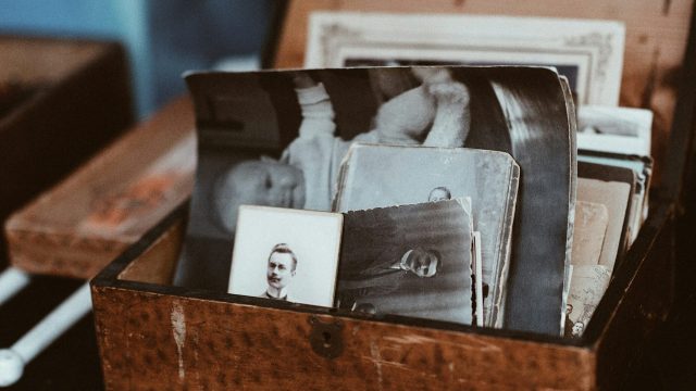 A wooden box filled with assorted old black-and-white photographs and postcards.