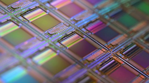 Close-up of a colorful microchip wafer with geometric patterns and reflective surfaces.