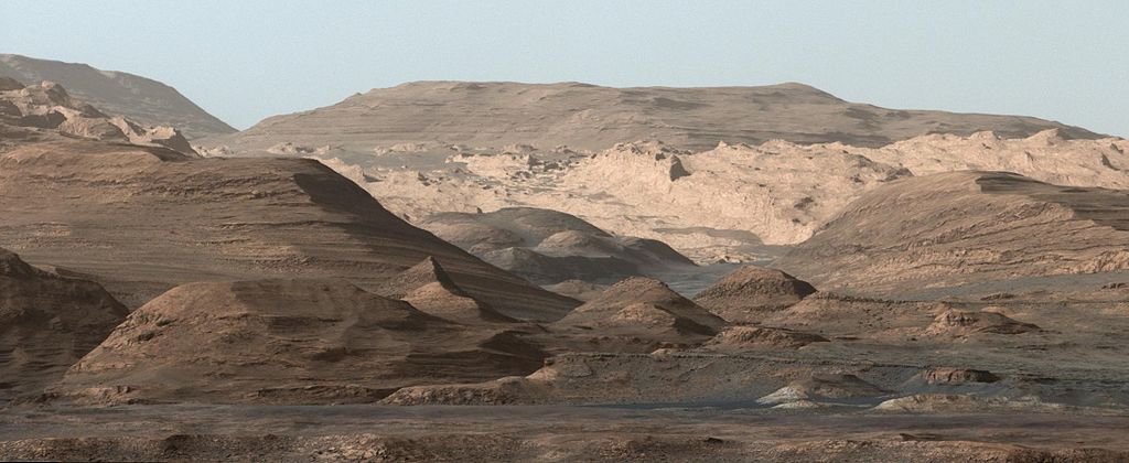 Rocky Martian landscape with hills and layered formations under a clear sky.