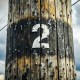 Close-up of a weathered wooden utility pole, marked with the number "2," standing resolute against cloudy skies—a testament to the enduring habits of nature and time.