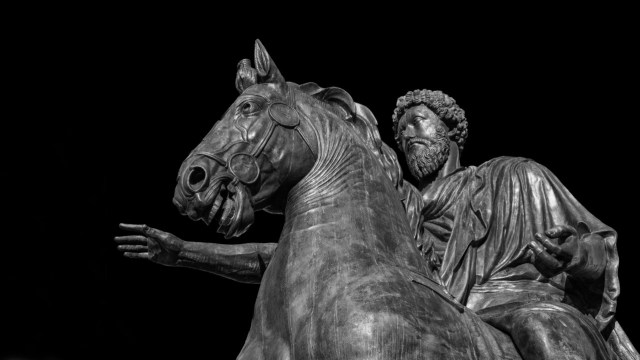 Bronze statue of a bearded man embodying stoicism, riding a horse with one arm extended forward, set against a black background.