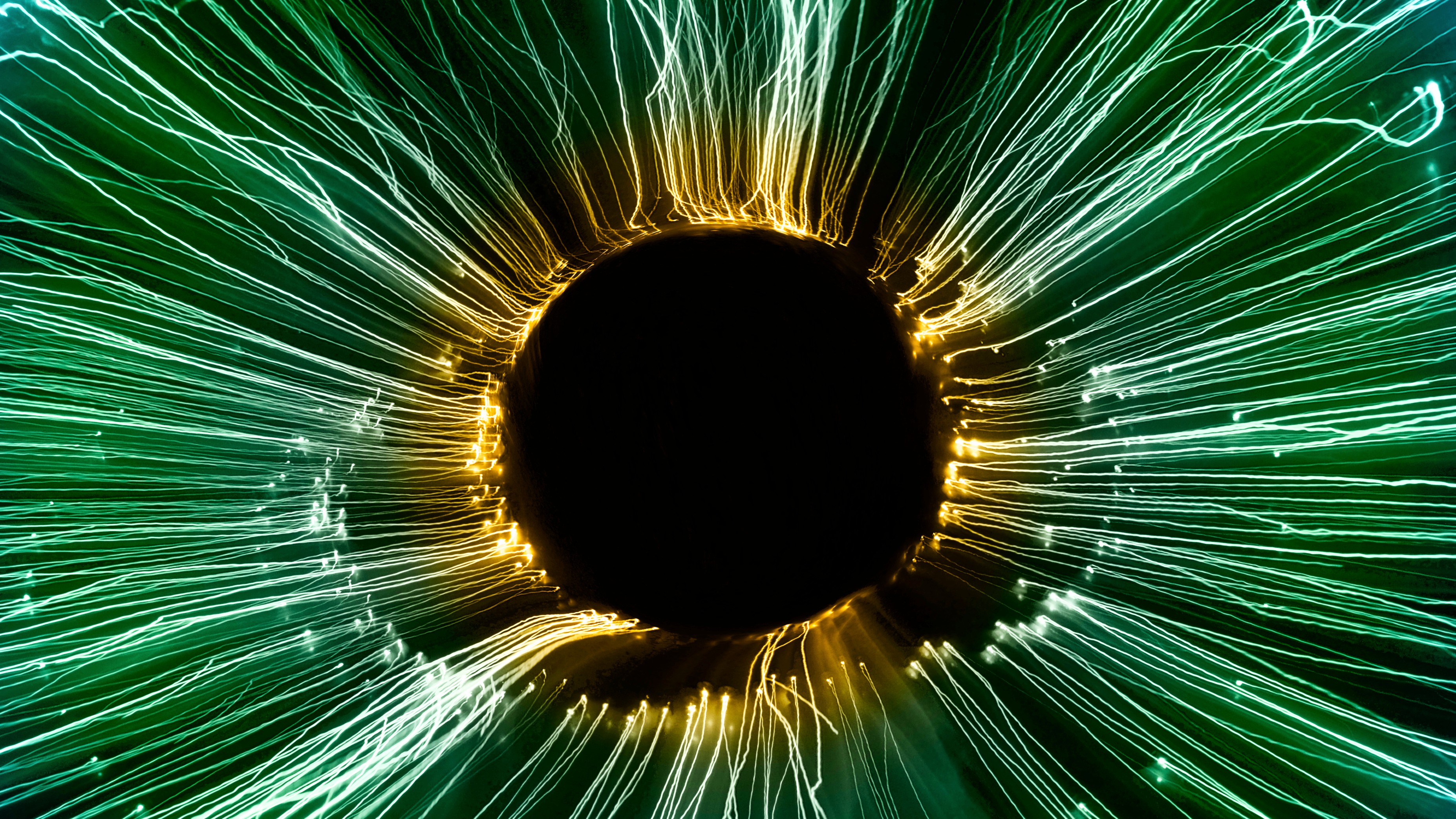 Abstract image of a dark central circle surrounded by radial green and yellow light streaks resembling an eye or vortex.