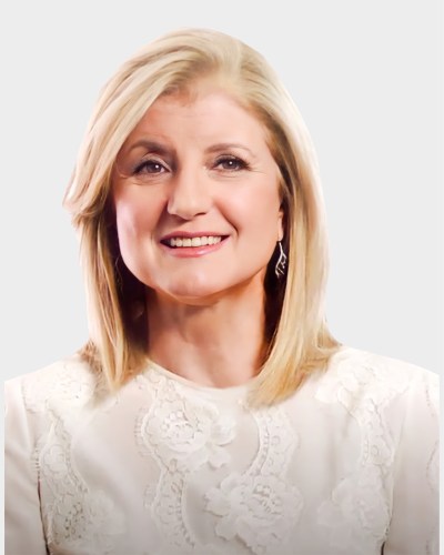 A person with shoulder-length blonde hair, smiling and wearing a white patterned top, set against a plain background.