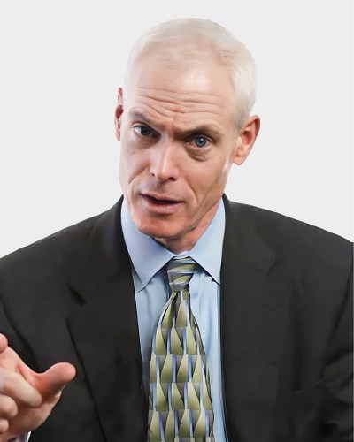 Man in a suit and tie gesturing while speaking, against a neutral background.