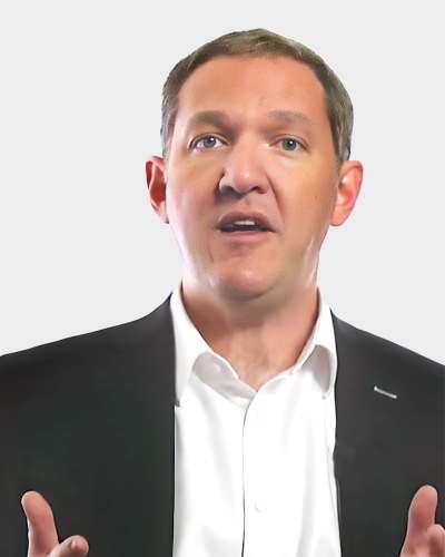 Person speaking while wearing a suit, set against a plain white background.