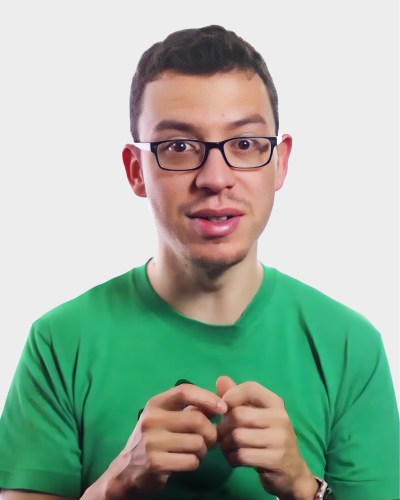 A man wearing glasses and a green shirt, gesturing with his hands against a plain white background.