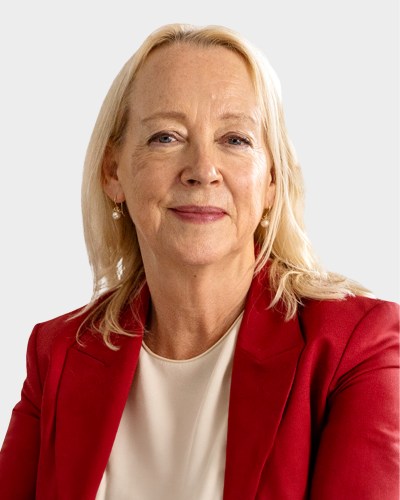 Smiling woman with shoulder-length blonde hair wearing a red blazer and white blouse against a plain background.