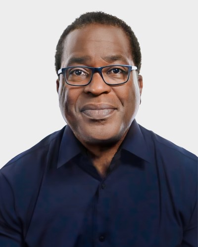 A person wearing glasses and a dark shirt smiles at the camera against a plain background.