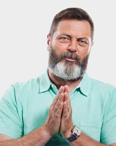 A bearded man wearing a light turquoise shirt clasps his hands together.