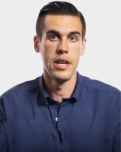 Person with short dark hair wearing a blue shirt against a plain background.