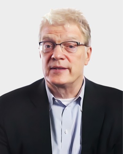 Man with light hair and glasses, wearing a black suit jacket and light blue shirt, looking forward against a plain background.