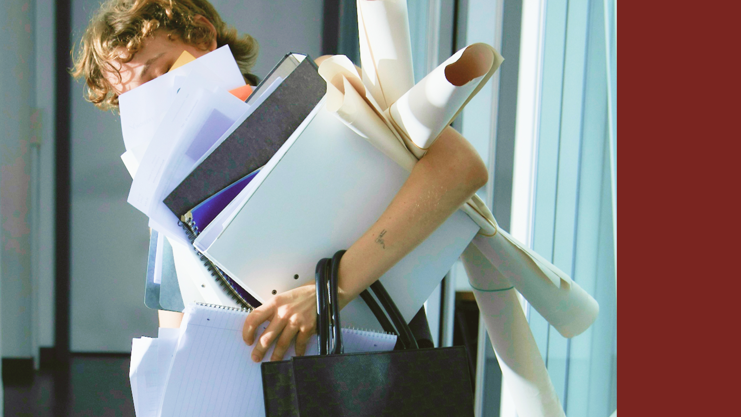 Arms burdened with a large stack of papers, folders, and rolled-up documents, a person exemplifies toxic productivity. Their black bag hangs precariously from their arm as they navigate the weight of their workload.