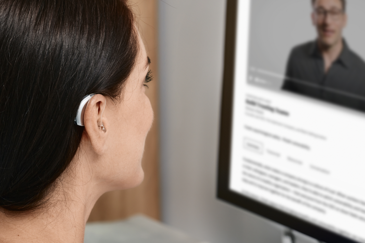 A woman with a hearing aid watches an online video on a computer screen.