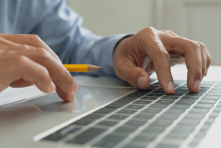 Person typing on a laptop keyboard while holding a pencil in their right hand.