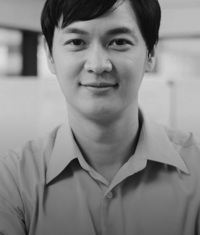 A person with short dark hair and a light-colored shirt smiles in a black-and-white indoor setting.