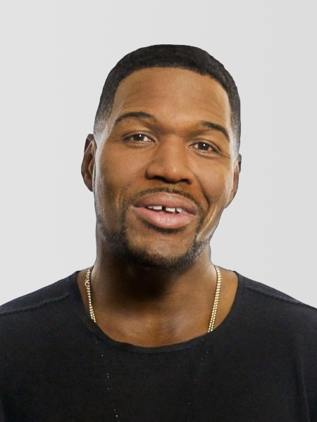 Michael Strahan wearing a black shirt and gold chain, smiling against a plain background.