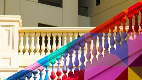 Colorful geometric design painted on the balustrades of a staircase against a pale building background.