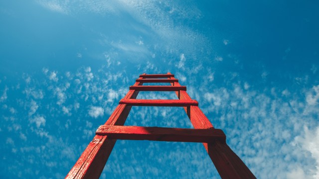 Red ladder extending upwards against a blue sky with scattered white clouds.