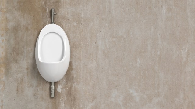 A wall-mounted white urinal against a beige concrete wall.