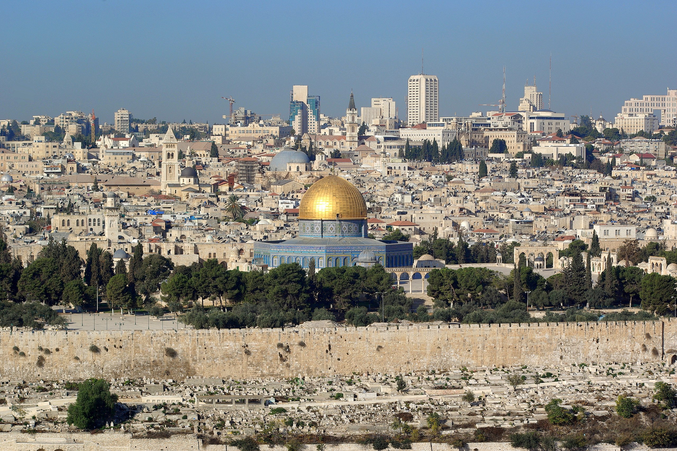 View of Jerusalem cityscape thrall to the mesmerizing Dome of the Rock, its golden dome gleaming amid historic buildings and lush trees.