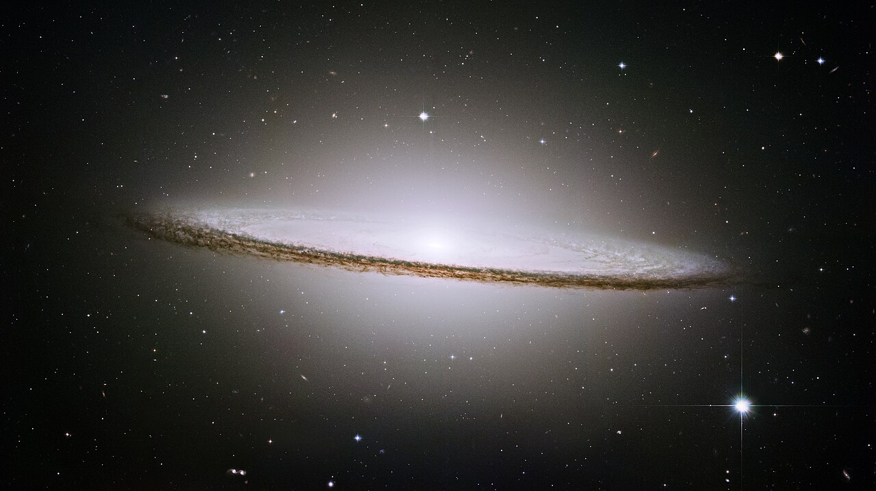 Image of the Sombrero Galaxy (M104) captured by JWST, showcasing its bright core and a prominent dust lane, surrounded by numerous stars in space.