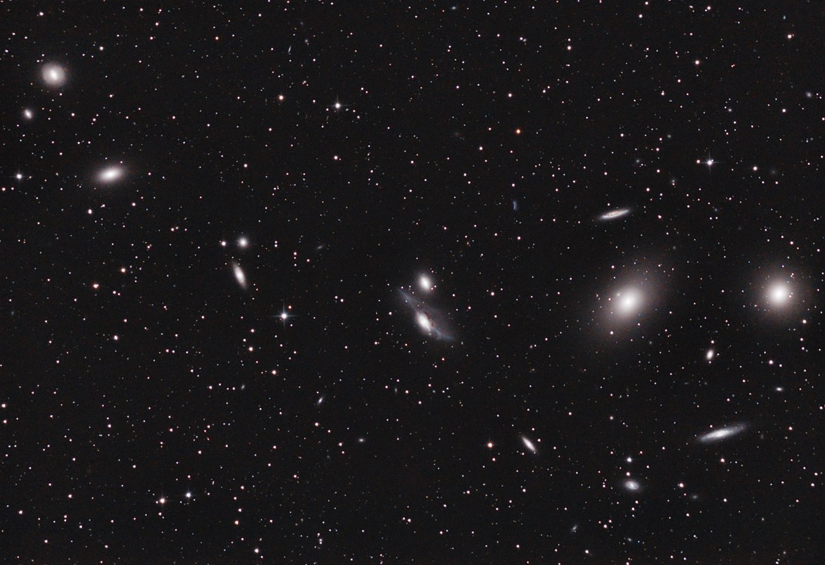 Wide view of a starry night sky with numerous galaxies and bright points of light scattered across a dark background.