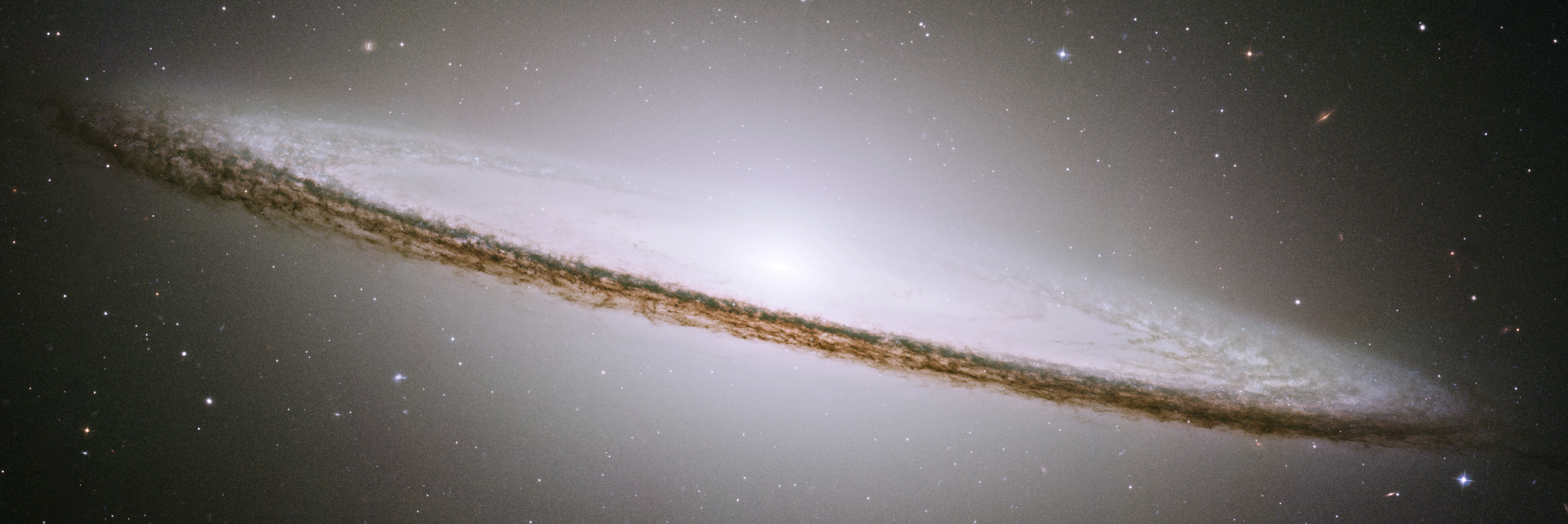 Image of the Sombrero Galaxy captured by JWST, showcasing a bright central bulge and a distinctive dark dust lane, all set against a backdrop of numerous distant stars and galaxies.