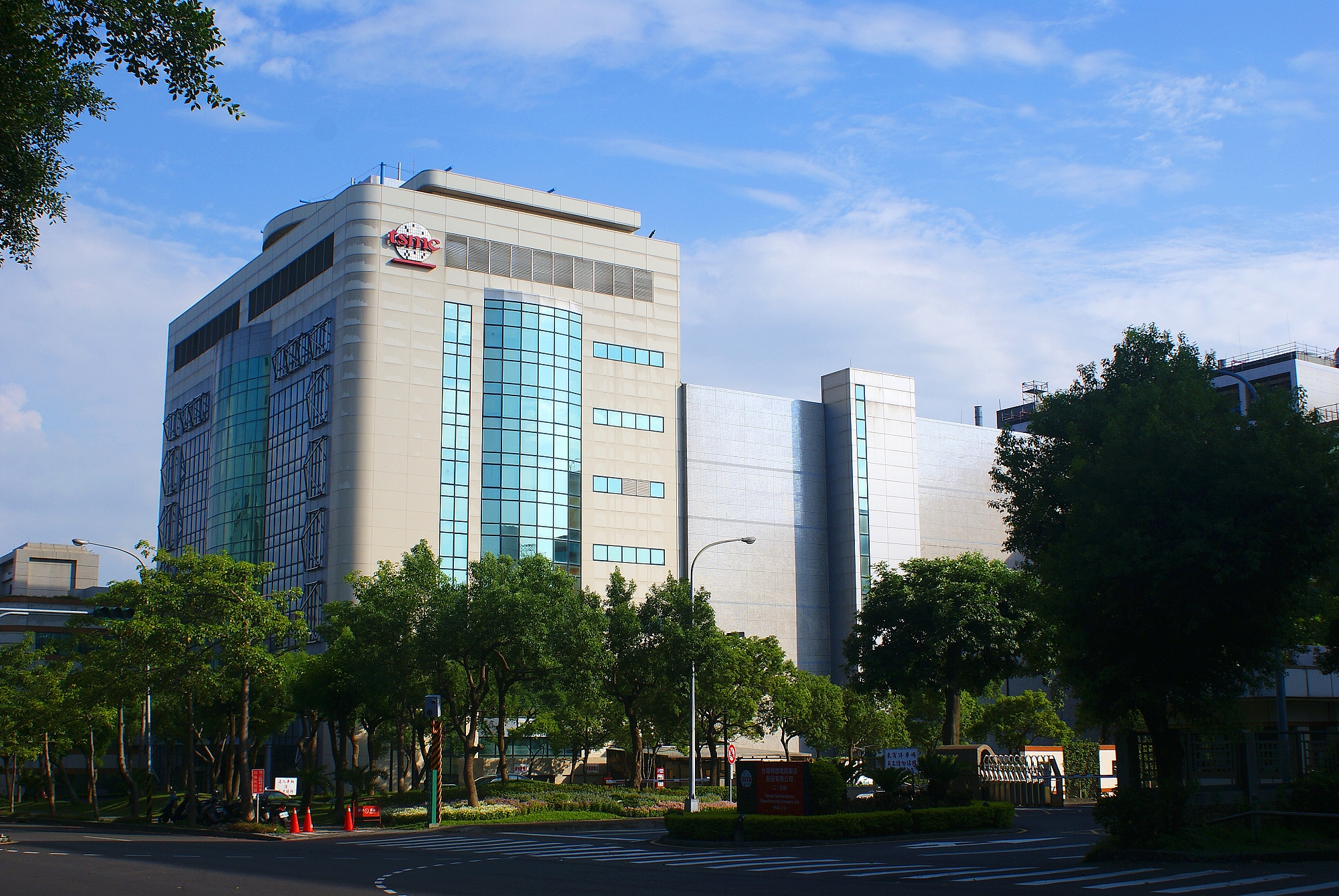 Modern office building with glass and concrete facade, surrounded by trees and a clear blue sky.