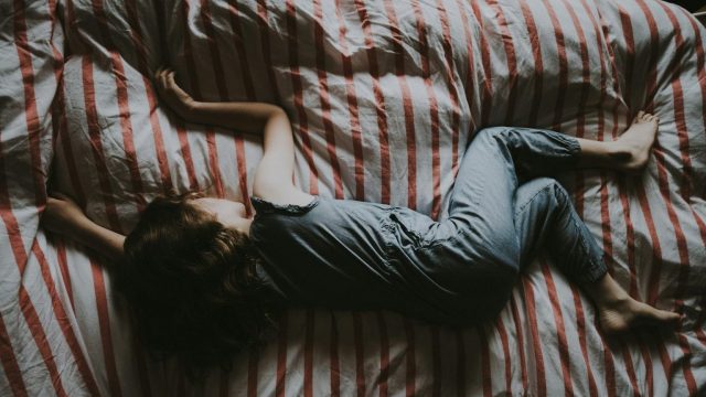 A child rests peacefully on a bed adorned with red and white striped sheets, wearing a blue outfit. It's as if their dreams are in sleep replay, caught in the tranquil rhythm of slumber, lying contentedly on their stomach.