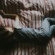 A child rests peacefully on a bed adorned with red and white striped sheets, wearing a blue outfit. It's as if their dreams are in sleep replay, caught in the tranquil rhythm of slumber, lying contentedly on their stomach.