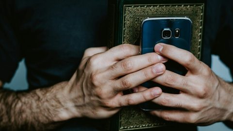 A person holds a smartphone and a book with an ornate cover, clasped together in both hands.